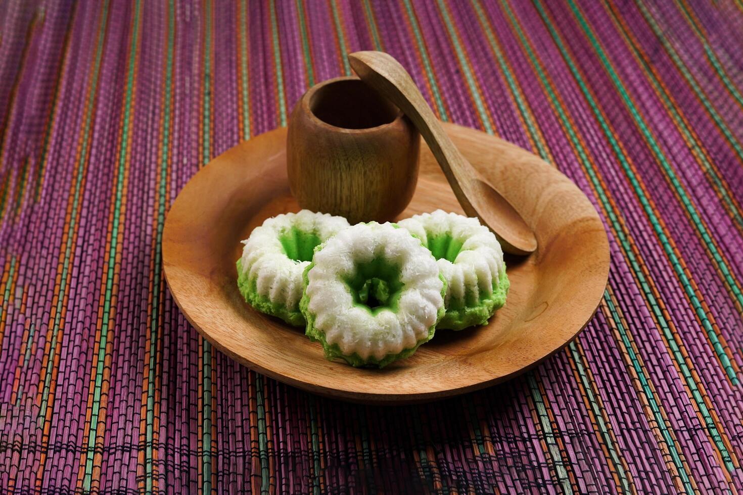 Putu Ayu is served on a wooden plate on a rainbow-colored base. It is a traditional dessert made from steamed rice flour and topped with grated coconut, a classic Indonesian cake photo