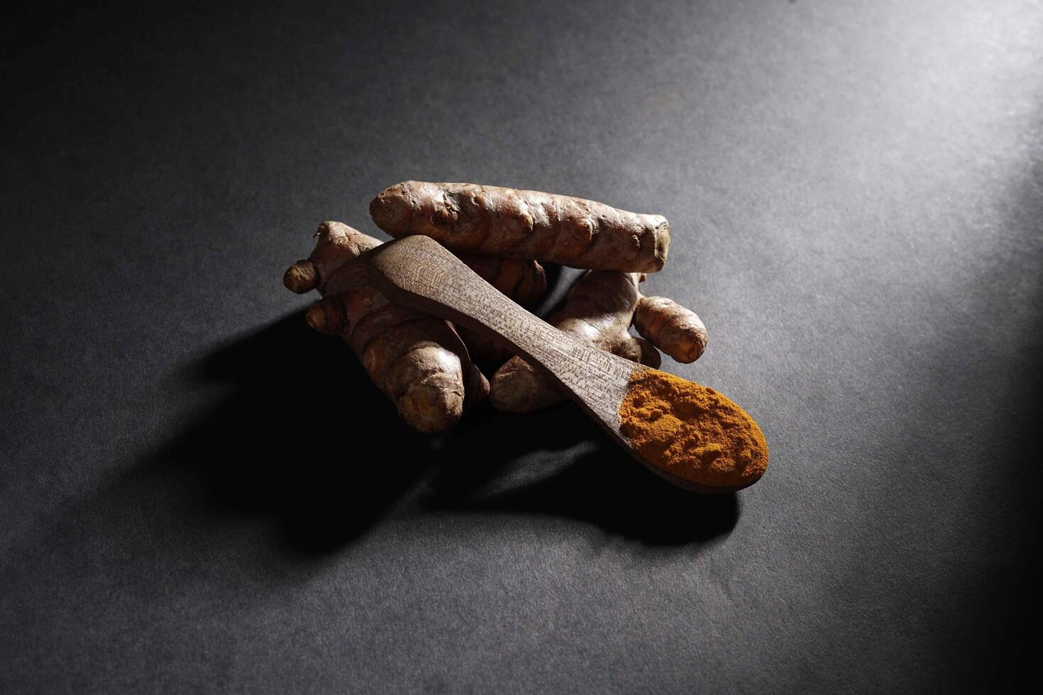 Fresh turmeric root and turmeric powder in wooden spoon, turmeric isolated on dark background, spice concept photo