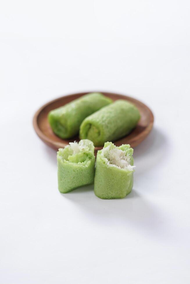 Traditional Indonesian food called 'Dadar Gulung' on a wooden plate, an elliptical cake filled with grated coconut and liquid palm sugar, isolated on a white background. photo