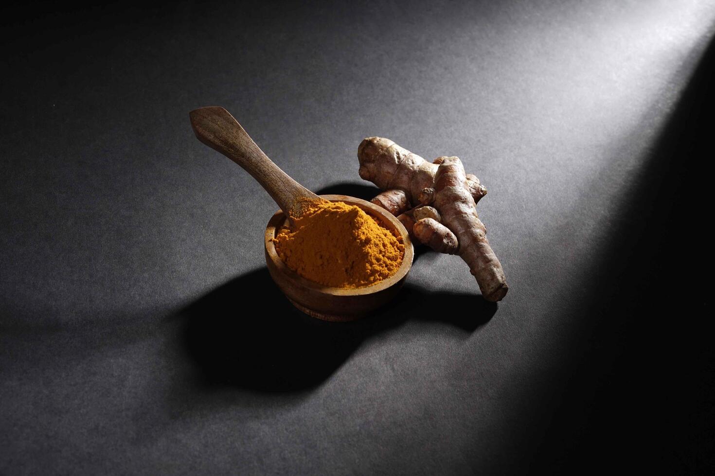 Fresh turmeric root and turmeric powder in wooden bowl, turmeric isolated on dark background, spice concept photo