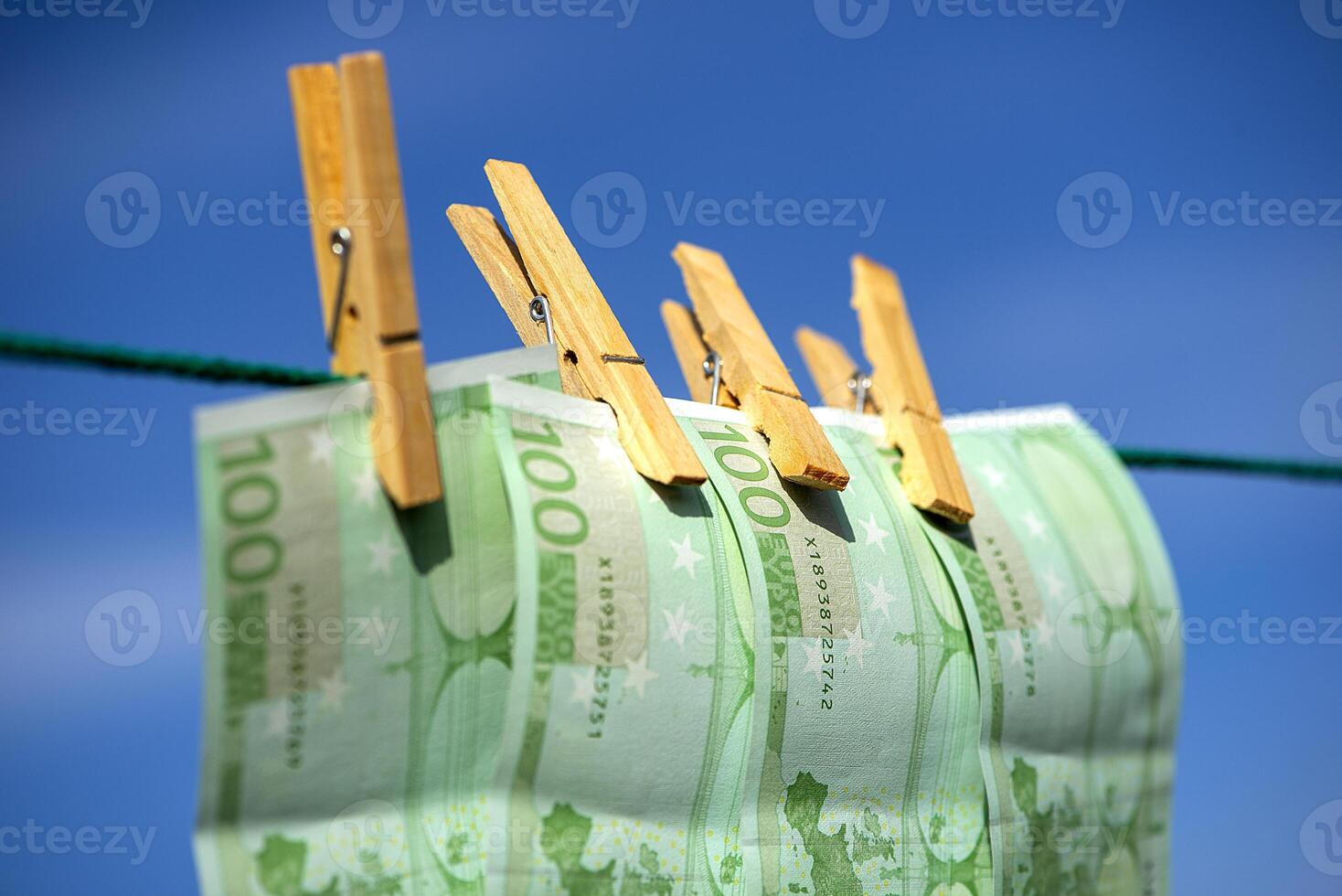 Hundred euro bills are hanging on clerical clips on a rope on the blue sky background. Closeup, selective focus photo