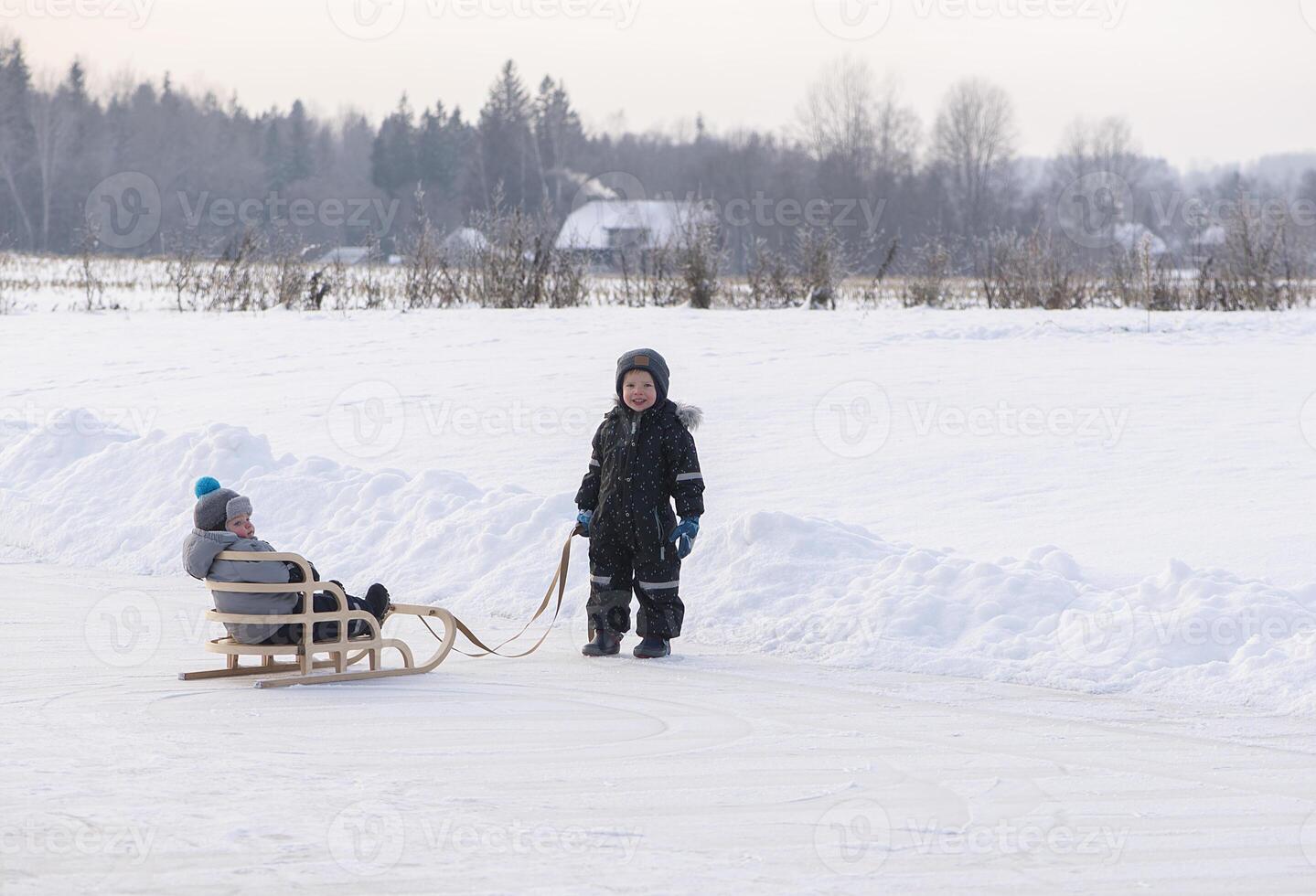 Two children on a winter lake, playing together with a sledge while snowing. Childhood happiness concept photo