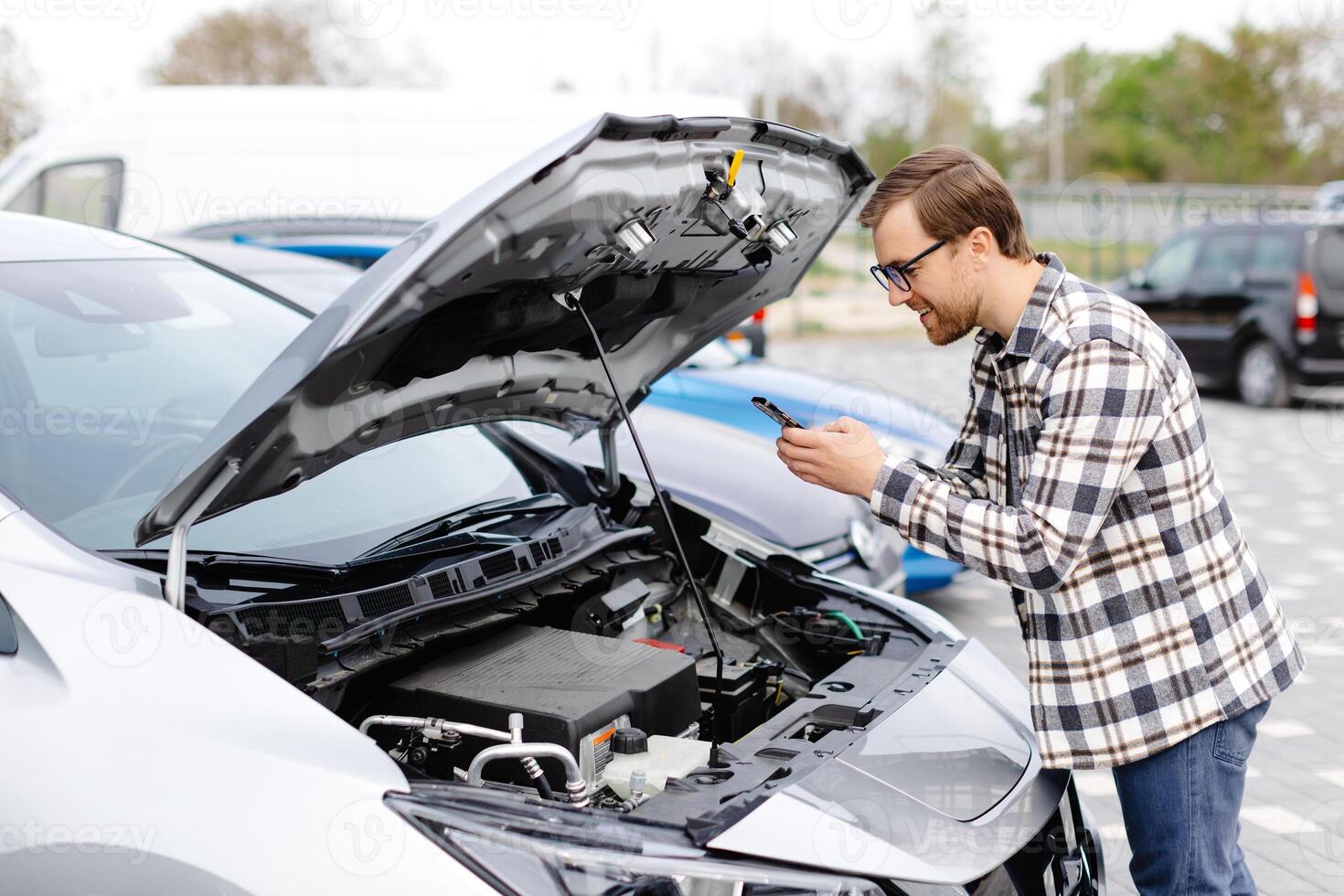 Young man checking under the hood of his car to figure out what the problem is. photo