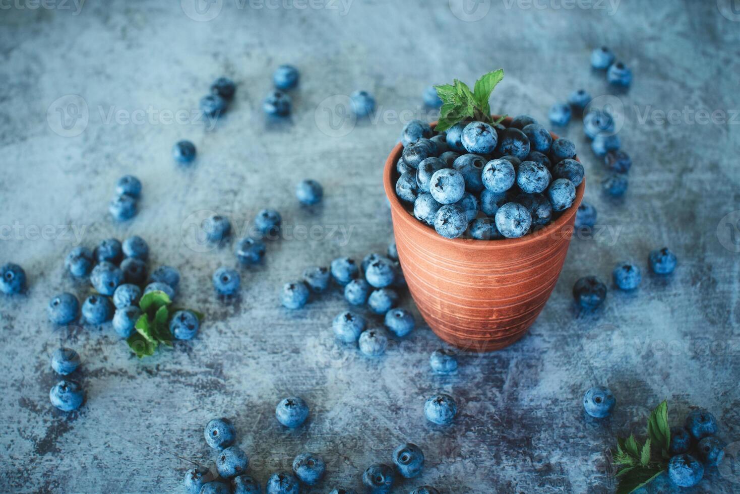 Ripe blueberries in a clay bowl and a pattern of berries on a dark background. Organic superfood and healthy berry. photo