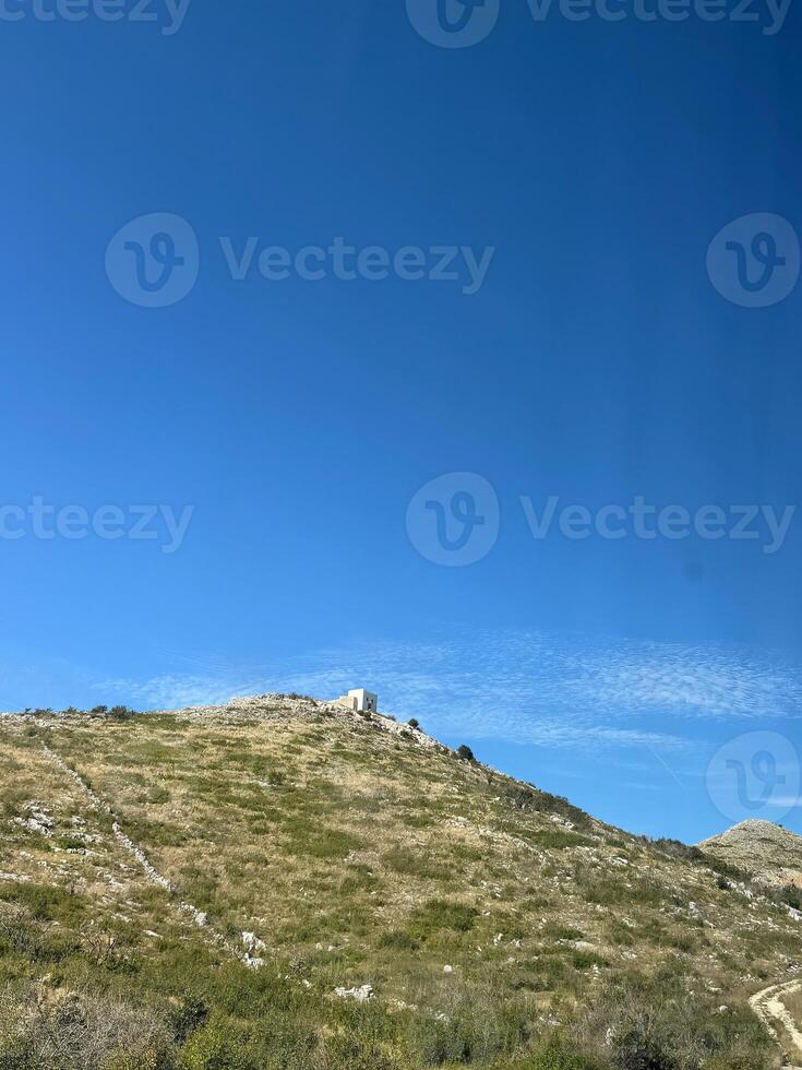 Grassy hill with a white house on it under a clear blue sky with minimal clouds. photo