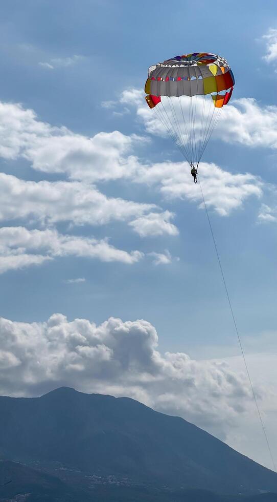 A person practicing parasailing in the blue sky next to the beach. Budva, Montenegro.26.09.24.High Quality Photos
