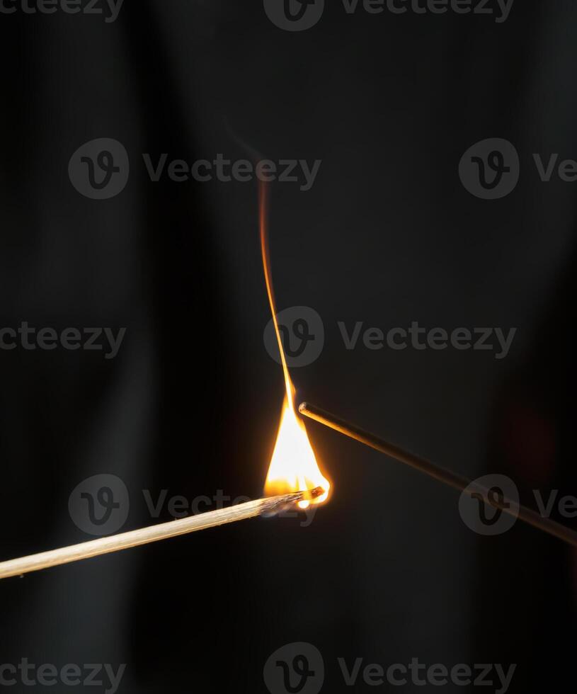 Burning match lights incense stick on black background, macro shot.long wooden match with burning head photo