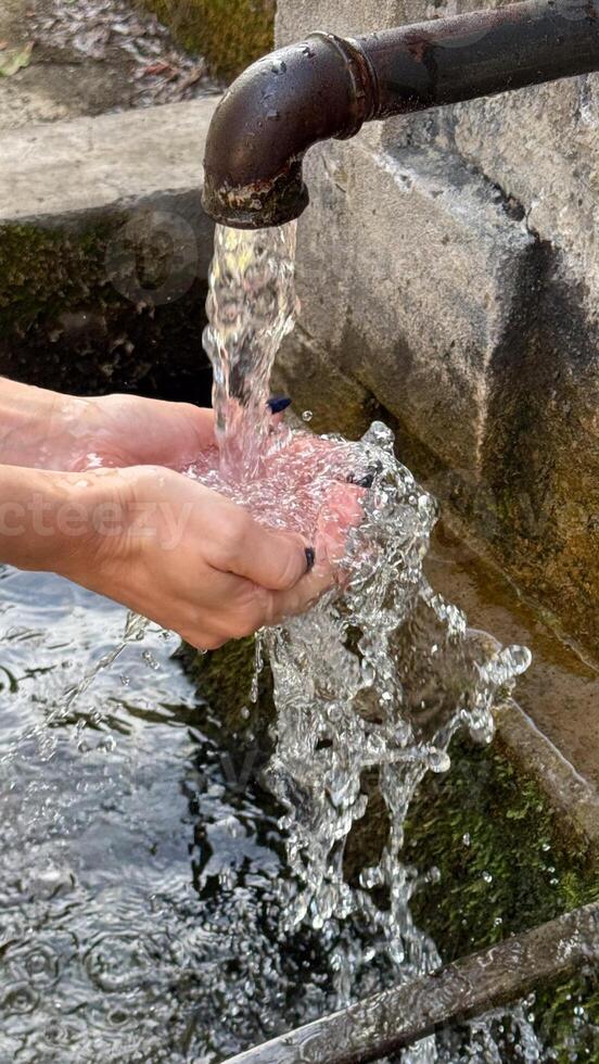 Hands under a stream of water from a metal outdoor faucet pouring into a stone bowl. freshness and nature. photo
