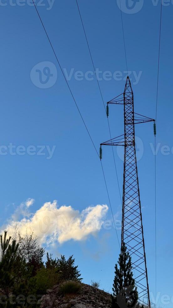 A tall power line tower stretches toward a clear blue sky with light clouds. nature and industrial technology. photo