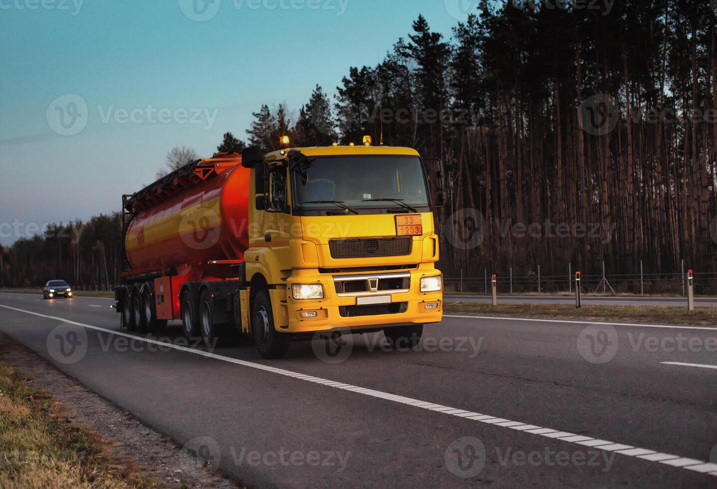 A truck carries a tank of combustible fuel on a highway against a forest and blue sky. The concept of transportation of dangerous goods on the road, license photo