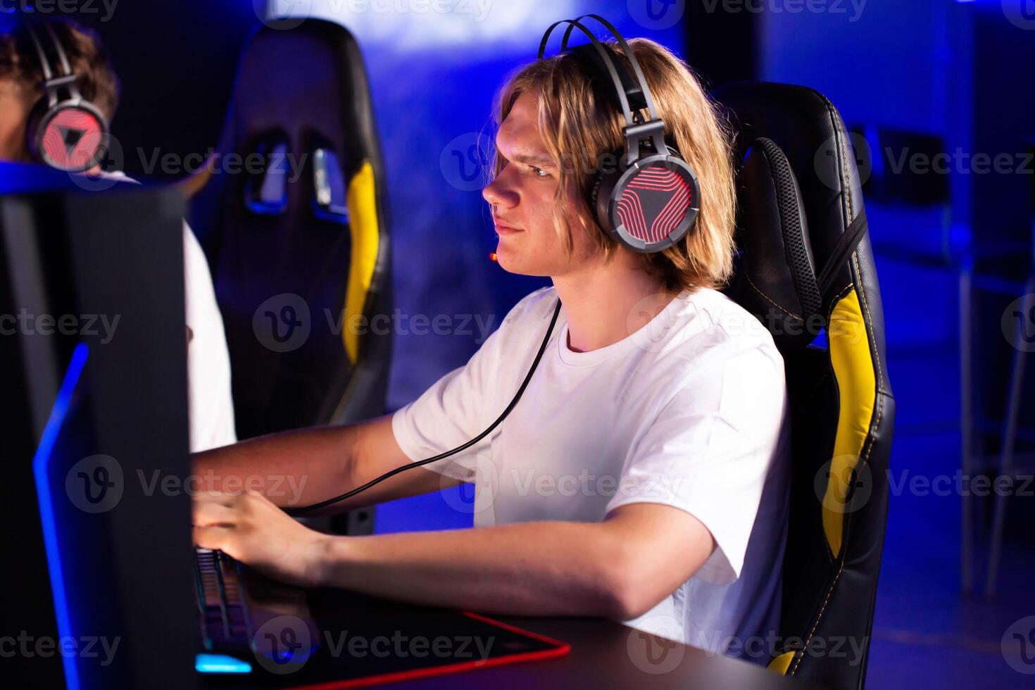Smiling laughing pimply teen gamer in headset playing PC game at computer club with team cyber sport tournament. E-sport championship. Multiplayer online real-time strategy first-person shooter photo