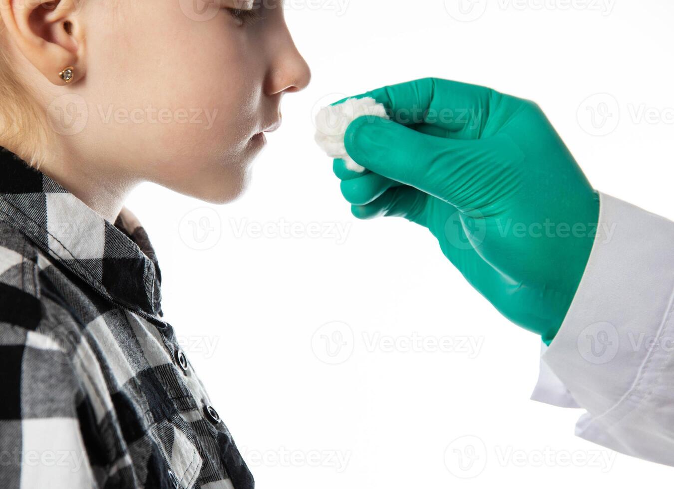 a doctor's hand in a medical glove holds a cotton swab with ammonia to the nose of a seven-year-old girl. White background. Fainting in children. Pre-fainting state. Copy space for text. photo