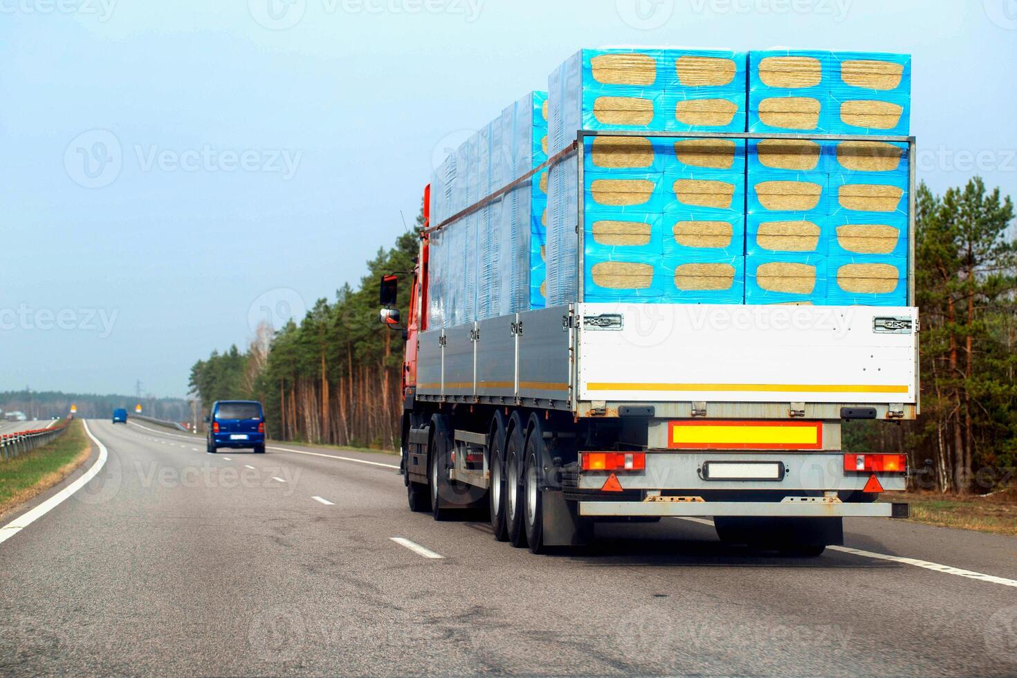 A truck with a semi-trailer transports a bulk load of insulation for construction along a country road in the spring. Copy space for text, industry photo