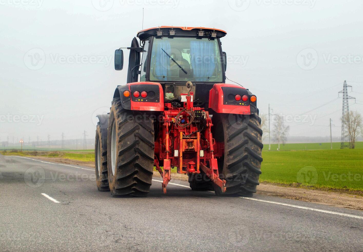 A modern red tractor drives on the highway against the background of fields. Concept of agricultural machinery on country roads. Copy space for text, industry photo