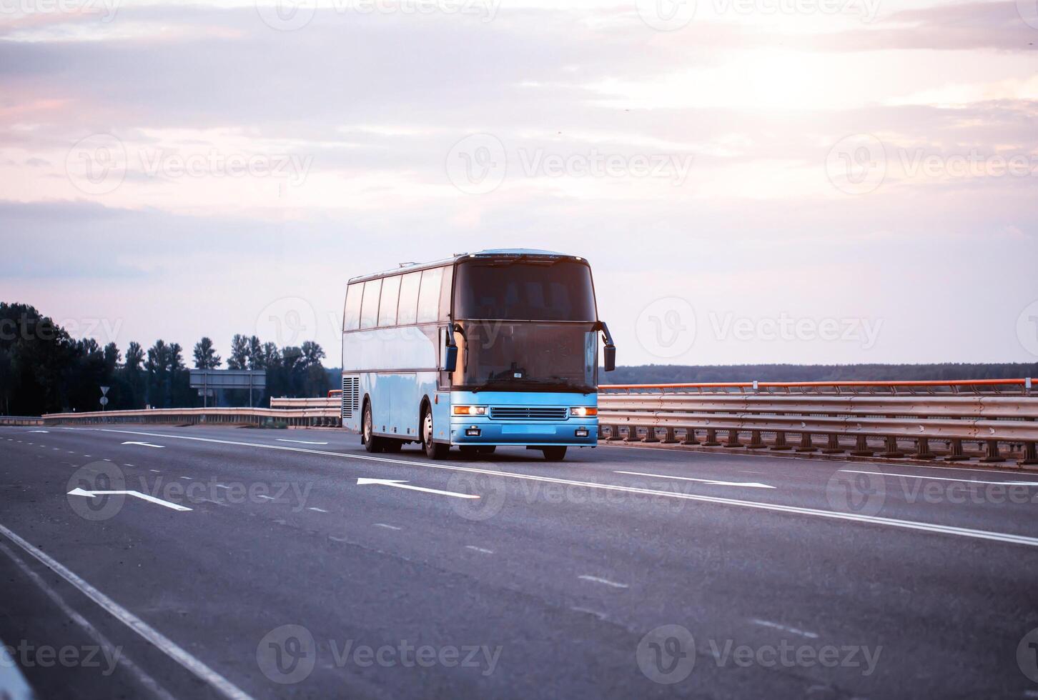 A blue comfortable bus carries passengers along the highway in the evening with the headlights on. The concept of travel and tourist tours from travel agencies. photo