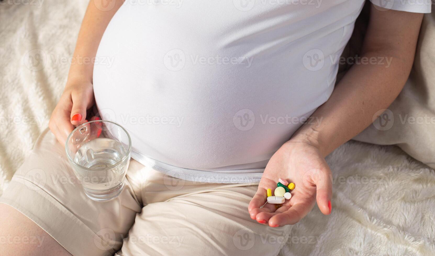 A pregnant girl holds pills in her palm and another glass of water. Concept of taking vitamins, iron and folic acid during pregnancy, close-up photo