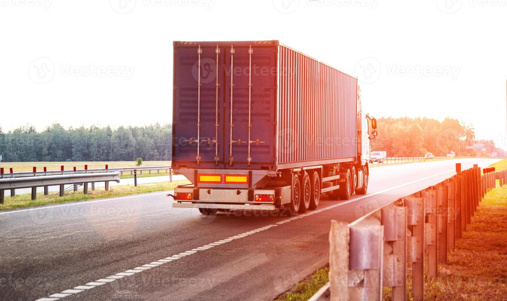 A container truck with a semi-trailer transports cargo from a port to another country along a highway in the summer against the backdrop of the sun. Logistics in cargo transportation photo