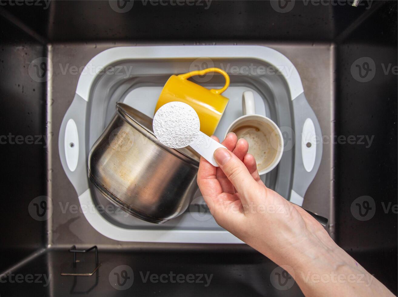 a measuring spoon with granules of environmentally friendly oxygen bleach is in the girl s hand. A modern means for cleaning and washing dirty dishes, close-up photo