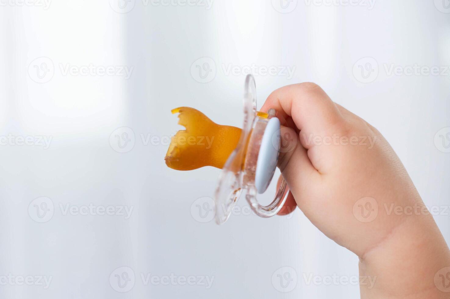 A baby's pacifier is chewed and torn in a baby's hand, close-up. Concept of teething in children, problems with bite. Copy space for text photo
