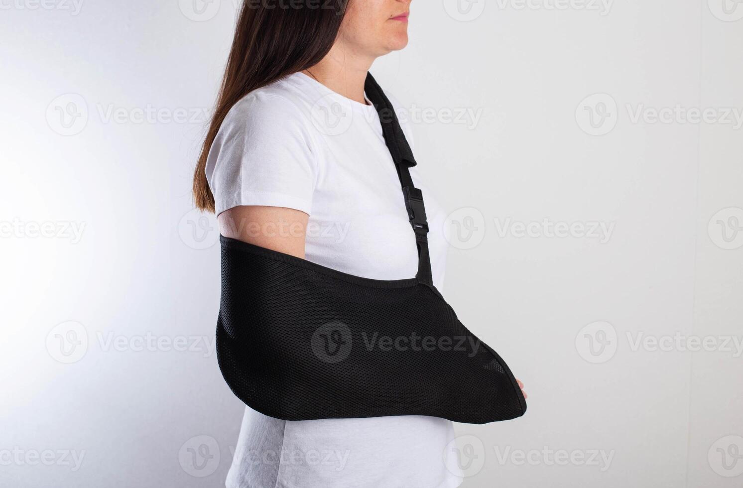 A girl in white with a fixing black bandage on her arm after an injury, a fracture of the radius and a sprain. Arm support bandage, hand immobilization photo