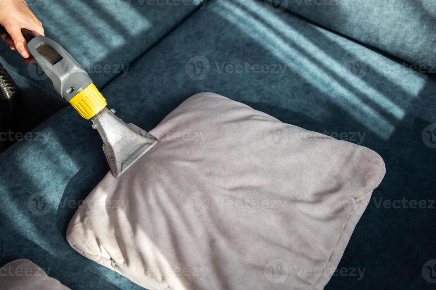A girl's hand with a professional washing vacuum cleaner cleans white pillows from dirt on the sofa. Cleaning services, copy space for text photo