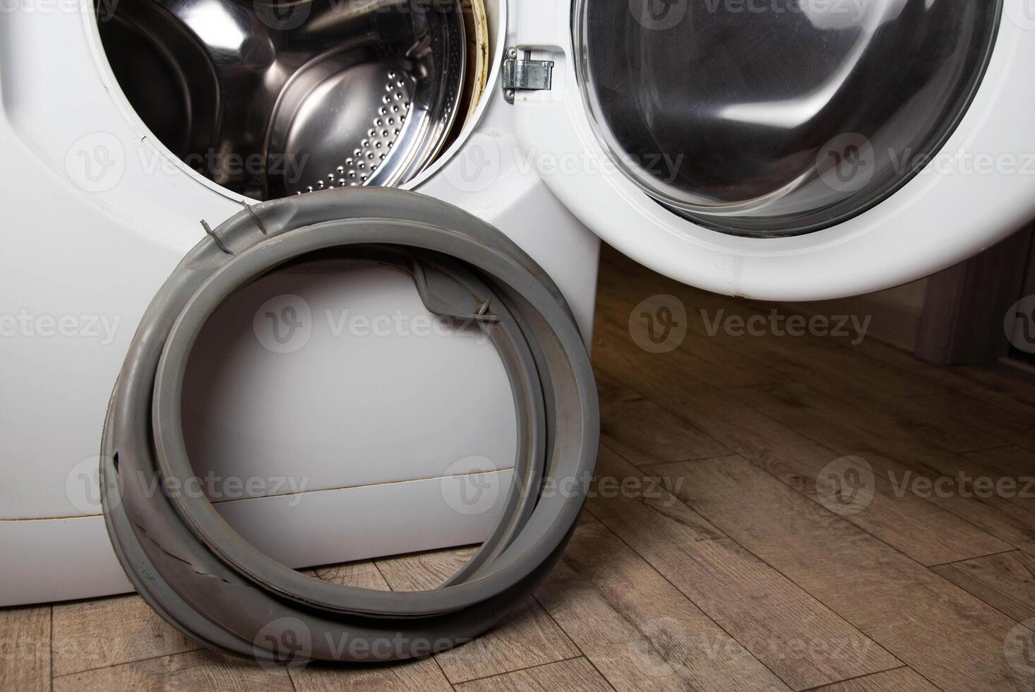 An old, torn, defective rubber hatch seal is standing near the washing machine. Spare parts replacement, industry. Copy space for text photo