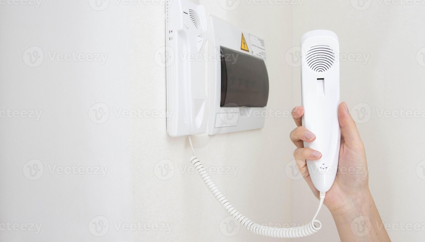 Intercom handset in a man's hand against the background of a white wall in the room. Security from unauthorized persons and theft in the apartment. Copy space for text photo