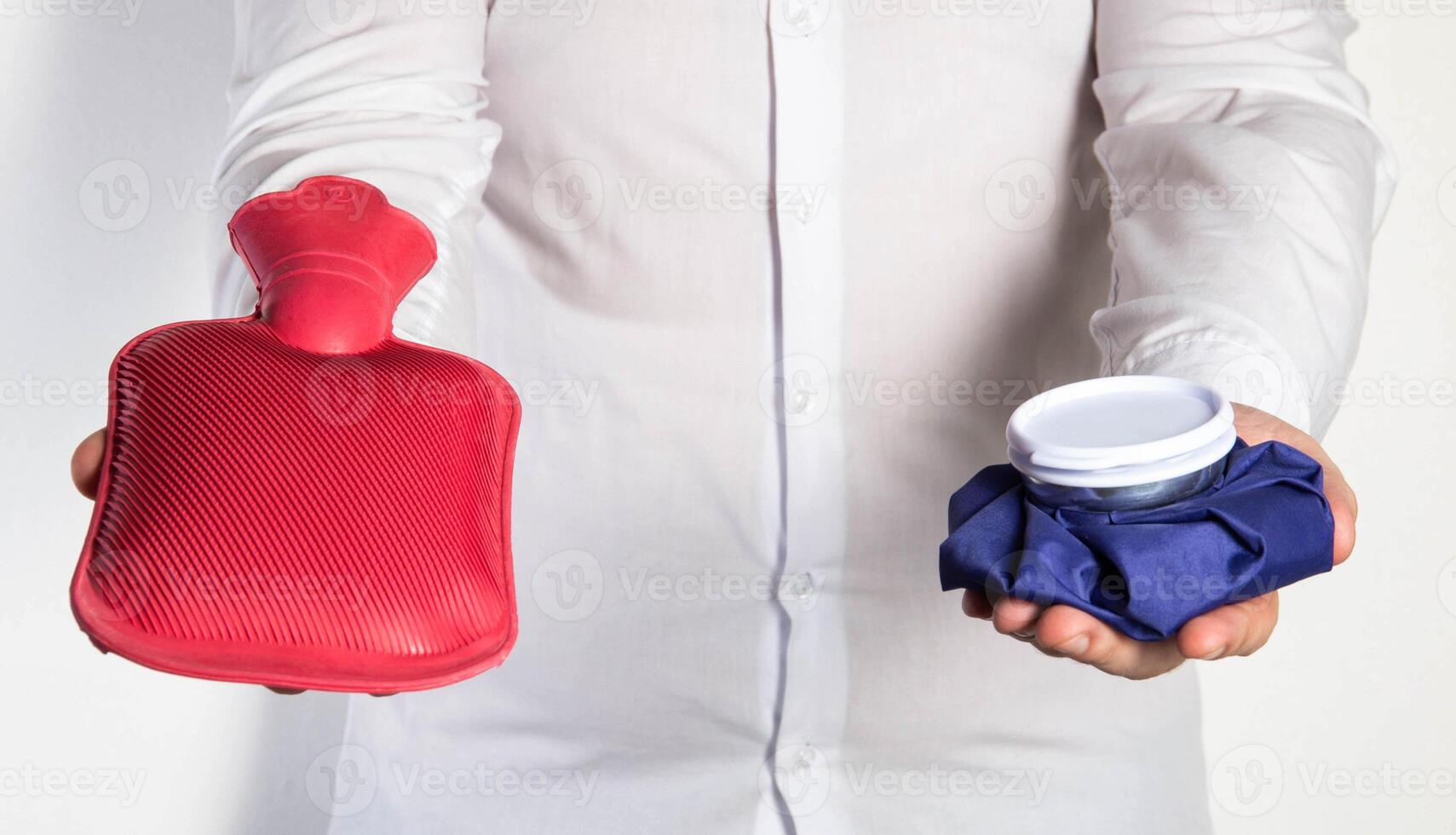 A man in a white shirt holds an ice bag and a red medical heating pad for hot water. The concept of heat and cold treatment. First aid for pain and inflammation photo