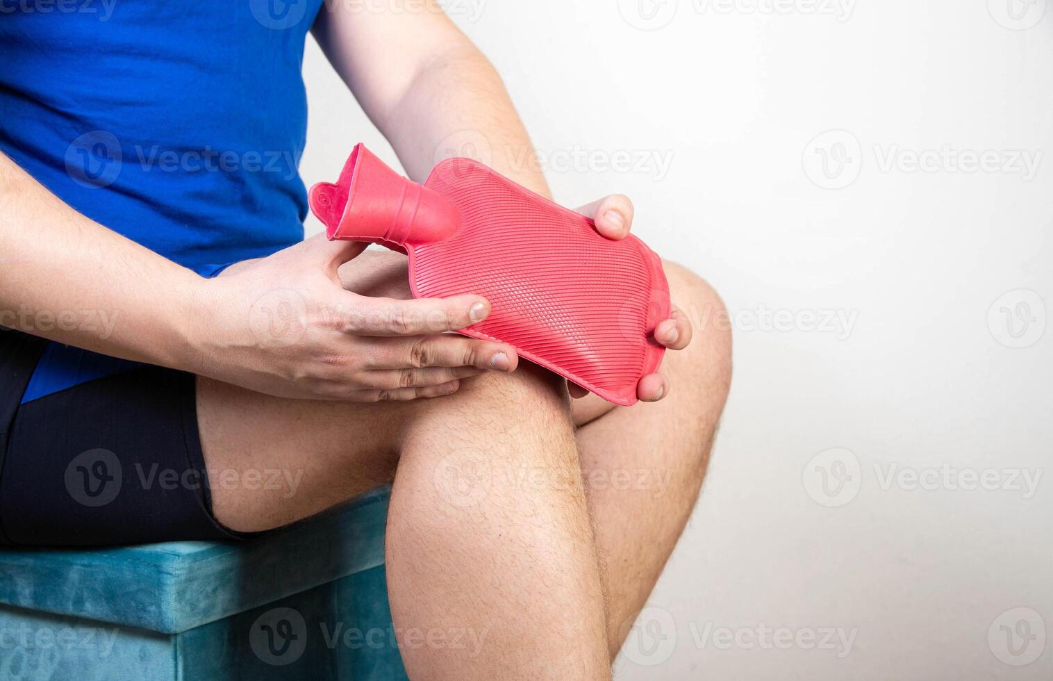A man attaches a medical heating pad with hot water to his knee. Treatment of knee sprains, pain and inflammation. Thermotherapy, copy space for text photo