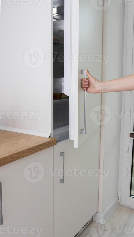 A man opens the door of a built-in refrigerator in the kitchen. Modern refrigerator placement technologies, renovation photo