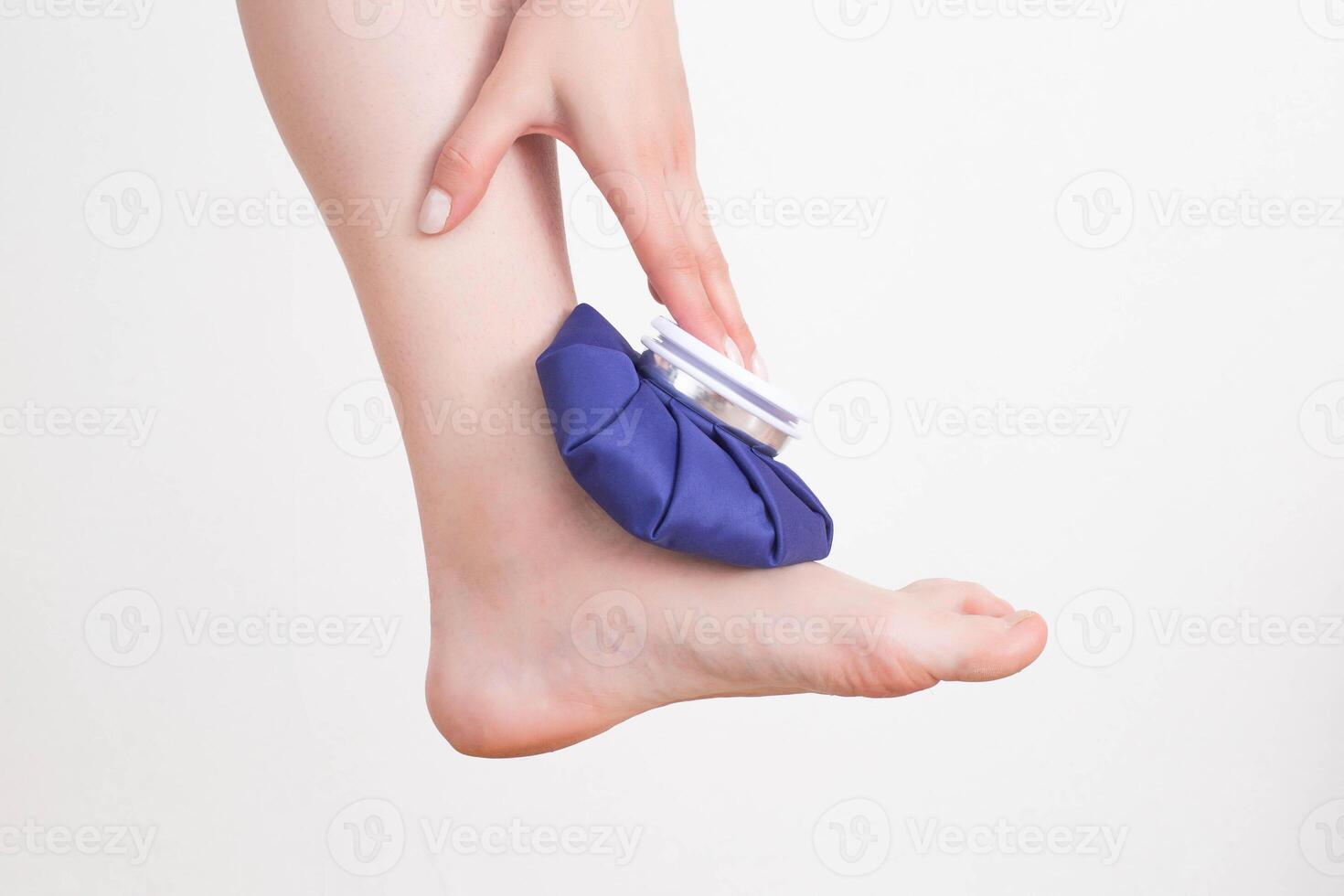 A girl applies a medical blue ice pack to the ankle joint to relieve pain and relieve swelling. Treatment of sports injuries and arthrosis of the leg joint photo
