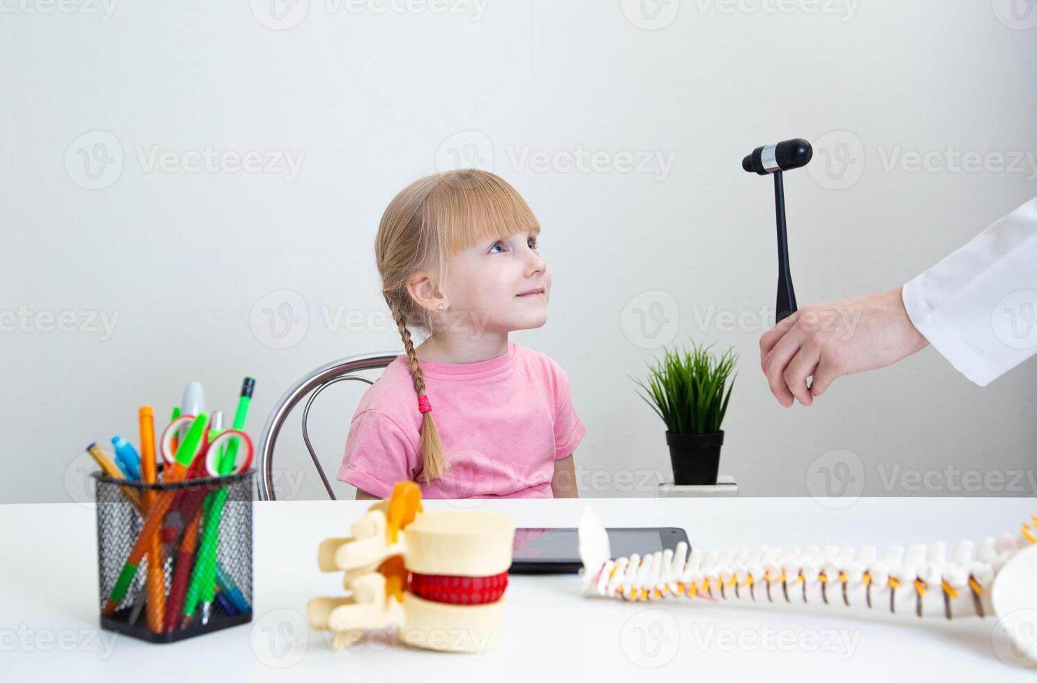 A neuropathologist checks the visual reflex of a 5-year-old girl. Asks to follow the neurological hammer with the eyes. Checking brain function in children. Copy space for text photo