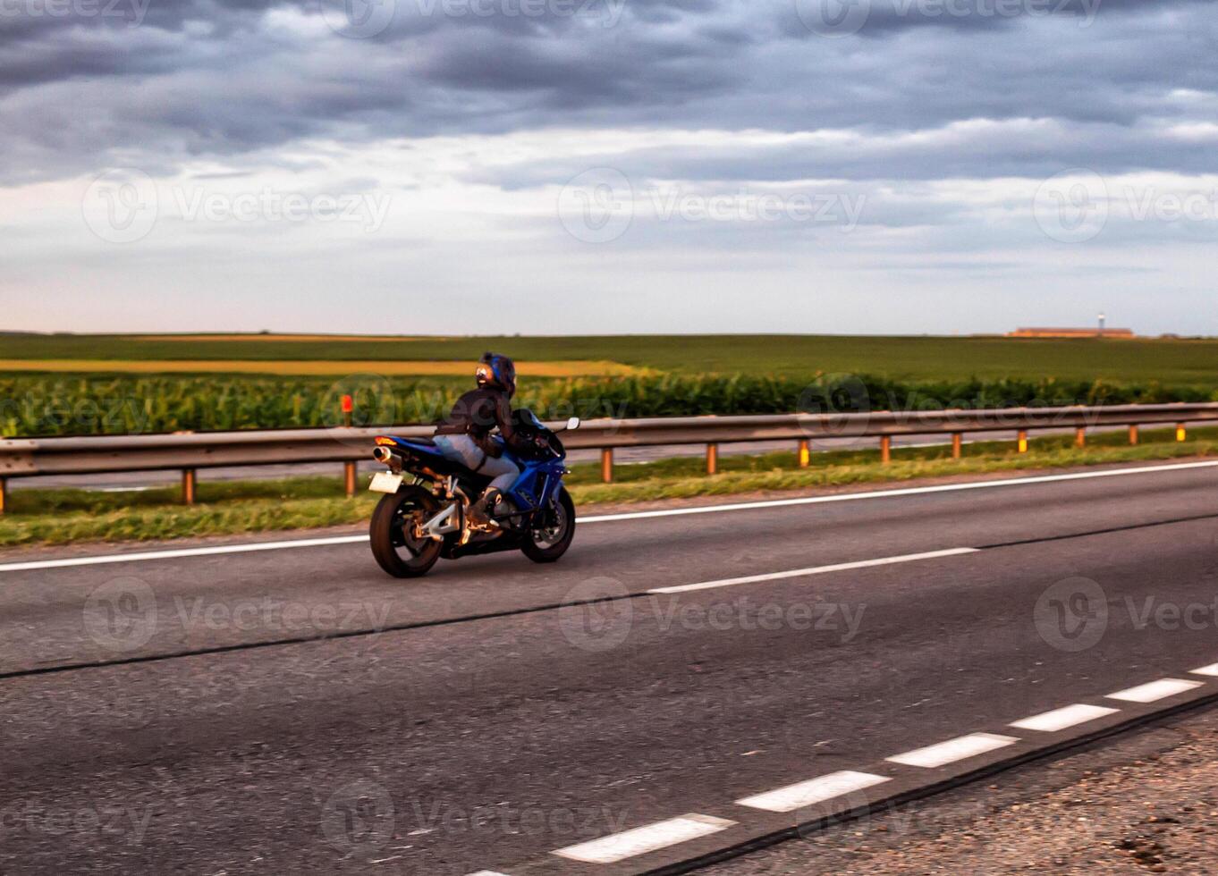 A biker on a sports motorcycle rides on a motorway in summer against the backdrop of clouds in the sky. Copy space for text photo