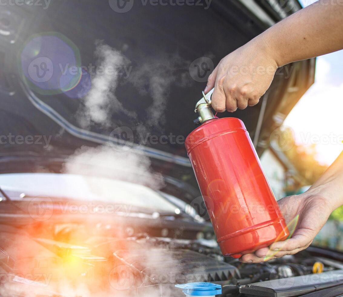The driver of the car directs a powder fire extinguisher at the engine compartment of the car in which there is fire and smoke. Car fire, background. Electrical short circuit photo
