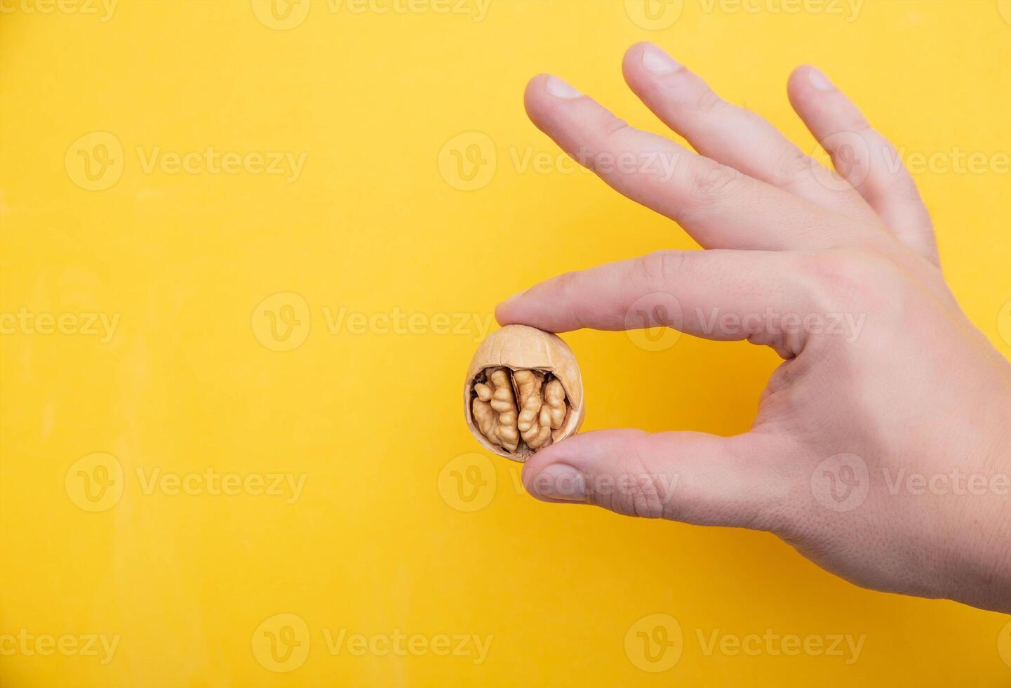 Walnut with a broken shell in the hand of a man on a yellow background. The concept of benefits for the human brain and mind. Copy space for text photo
