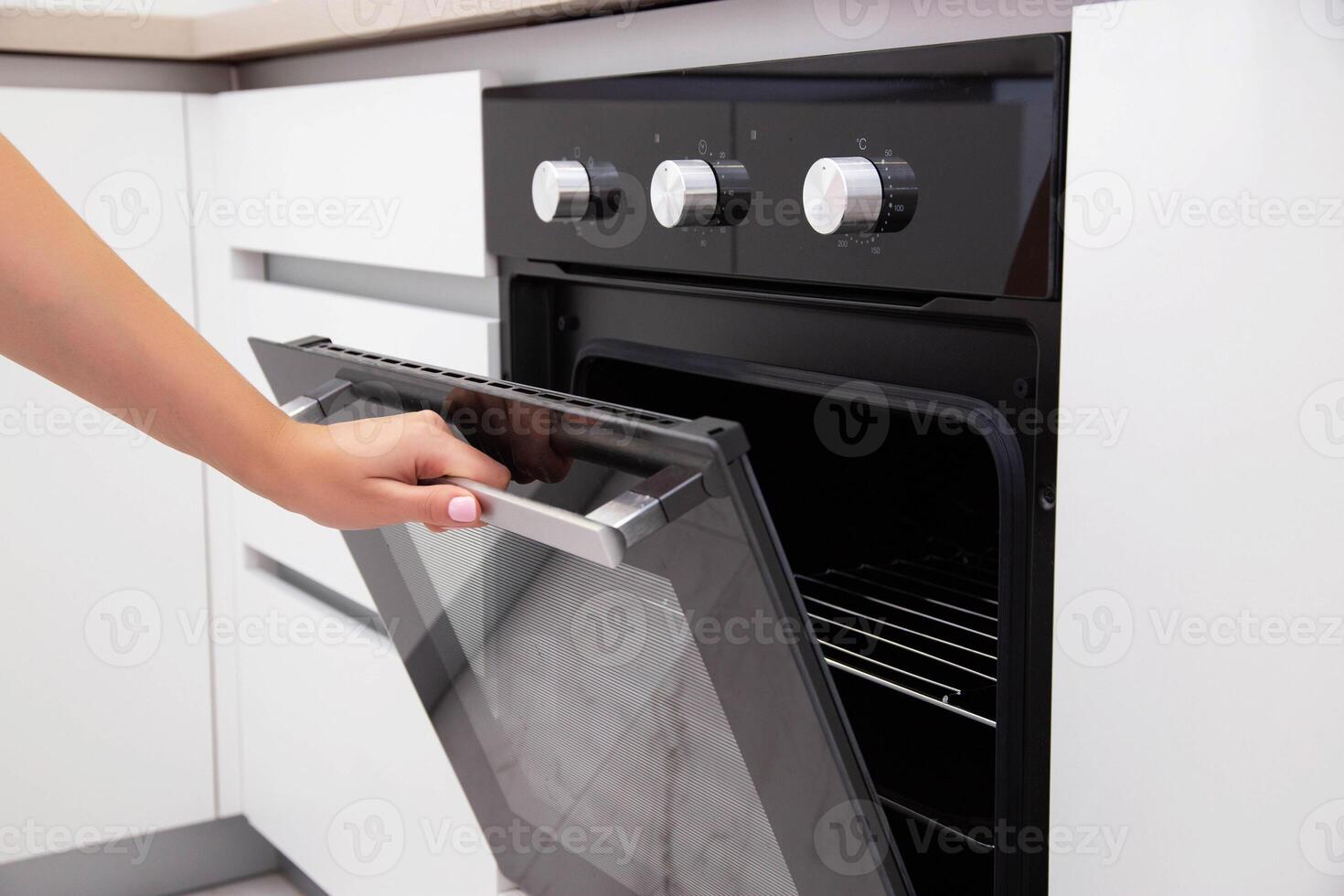A woman's hand opens the door of an electric convection oven. Built-in oven in the kitchen, energy consumption photo