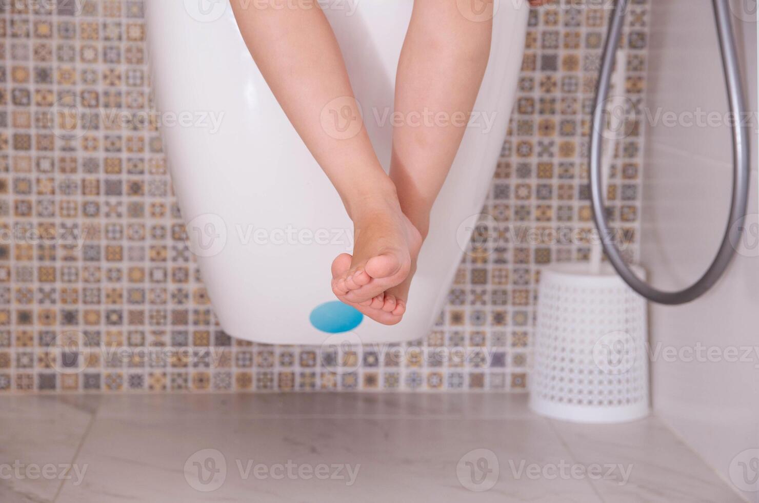 Legs of a child sitting in the toilet hanging from the toilet. Digestive disorders concept in children, rotavirus, intestinal microflora, close-up photo