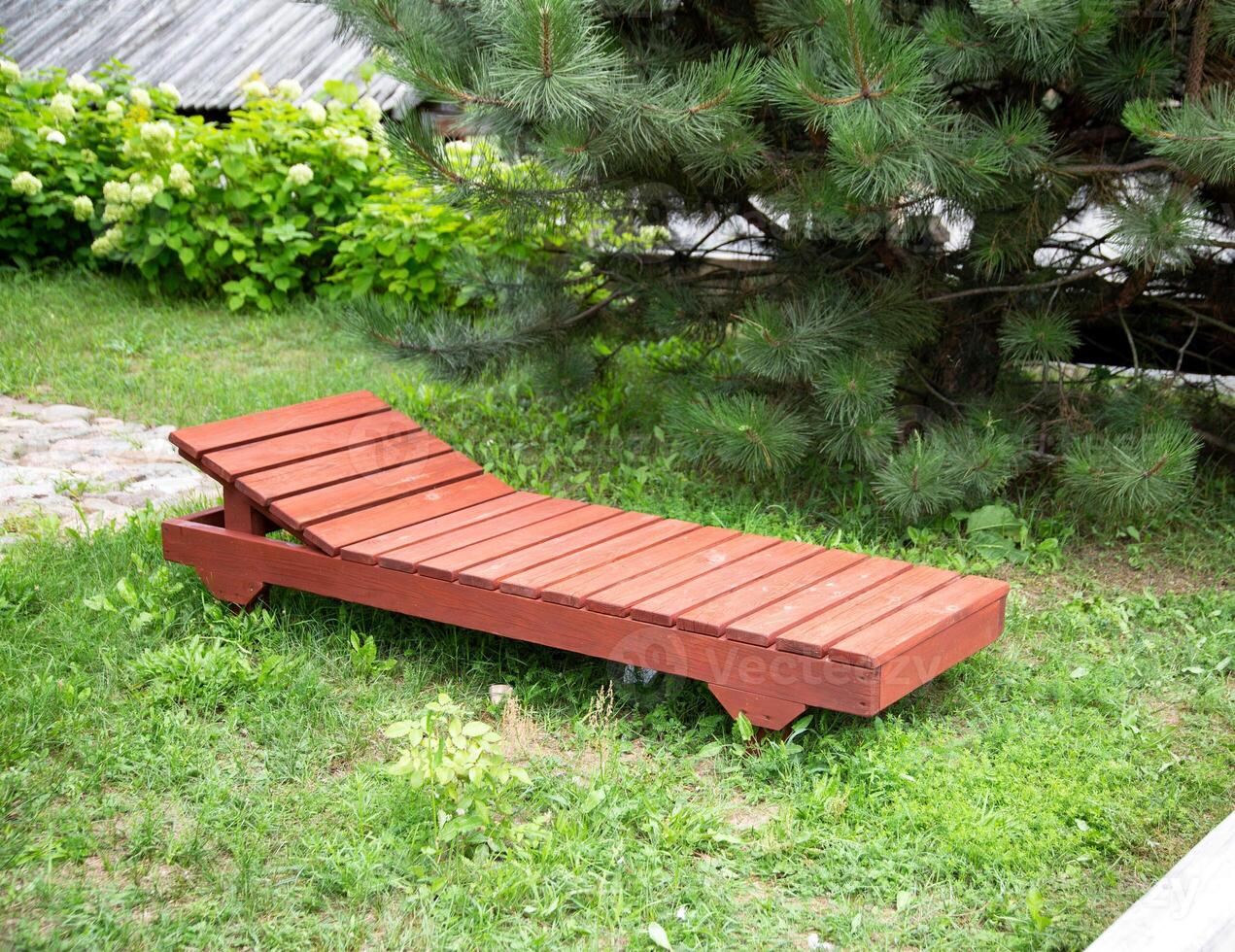 A wooden brown lounger stands on the green grass near the fir. The concept of recreation in the forest and in the country in the fresh air. Copy space for text photo