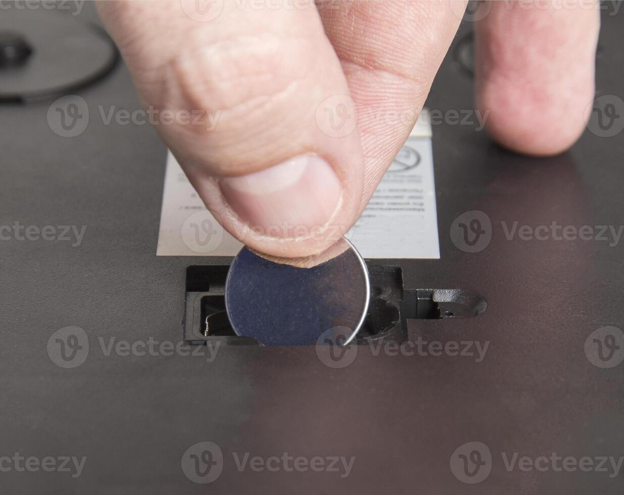 Installing a new round coin cell battery in an electrical appliance. Replacing a dead battery, macro. photo