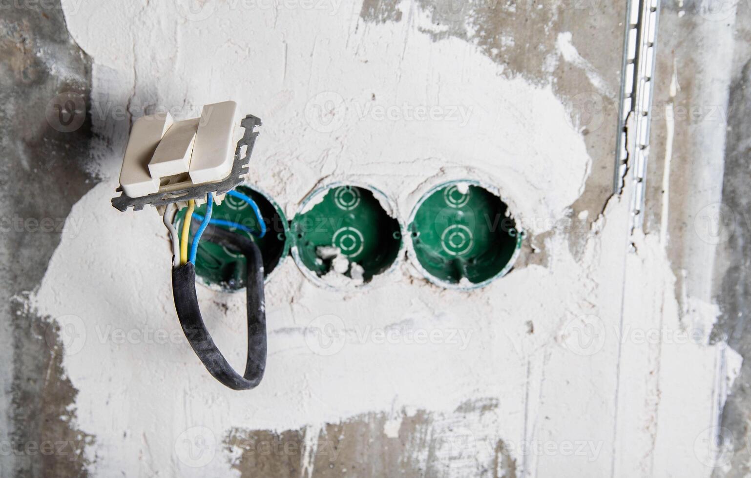 An electric switch hangs on wires from socket boxes built into a concrete wall. The danger of electricity photo