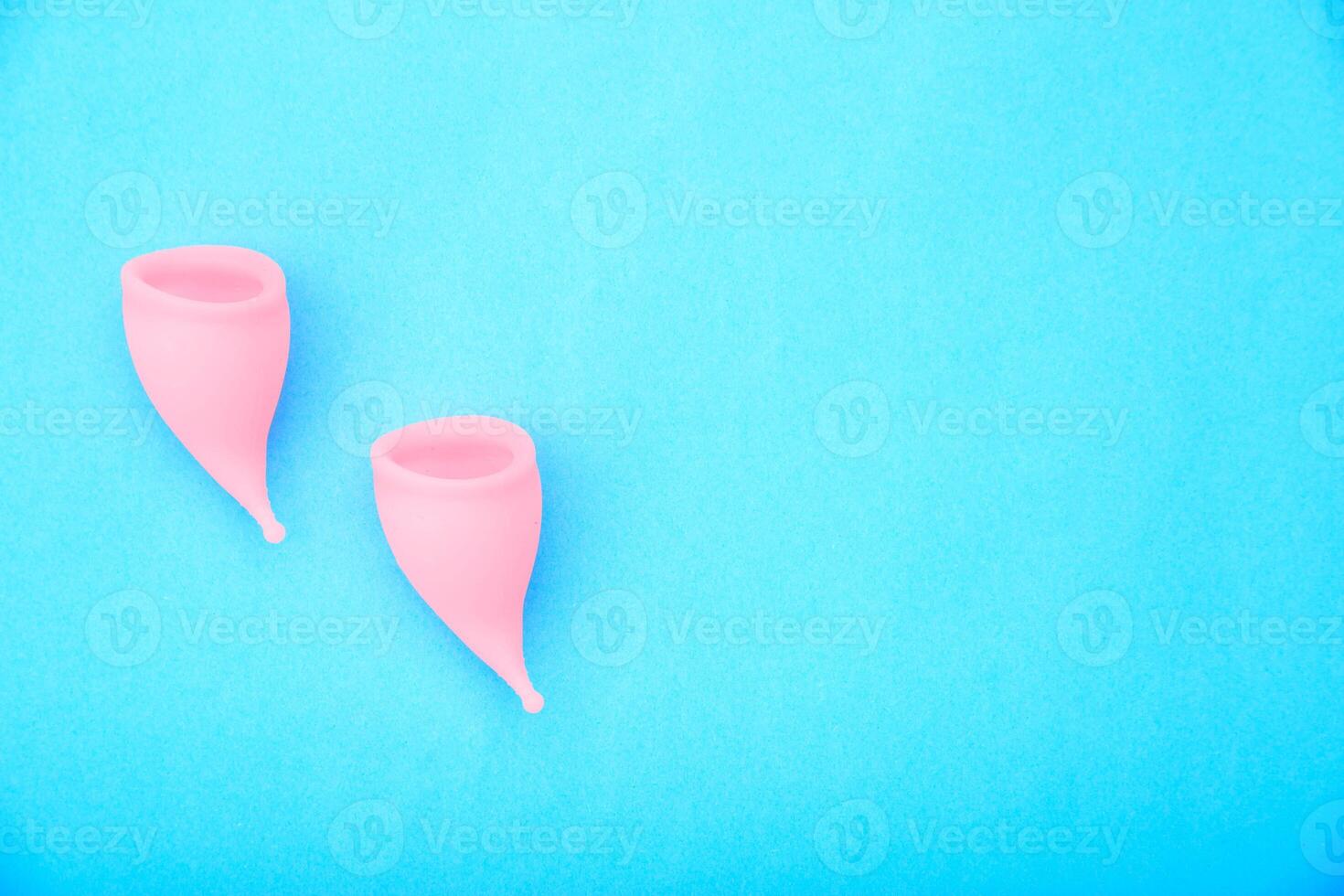 Two pink vaginal cups for girls to collect discharge during menstruation on a blue background. Replacement of female pads and tampons, close-up, gynecology. Copy space for text photo