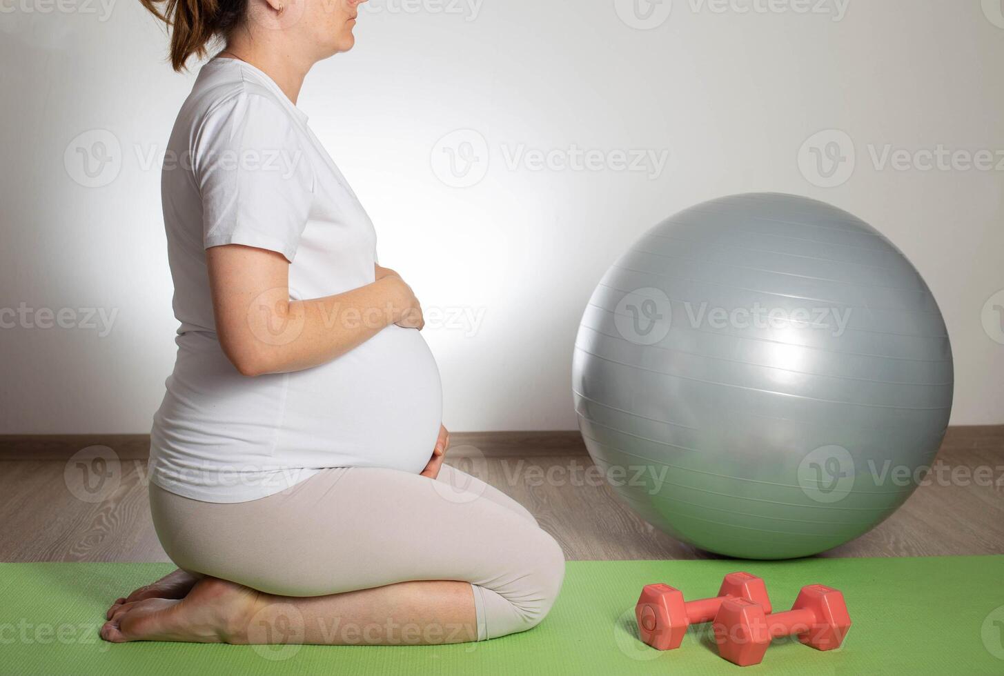 A pregnant girl goes in for sports in the 3rd trimester of pregnancy. Fitness and Pilates. Women's health. Exercises with dumbbells. photo