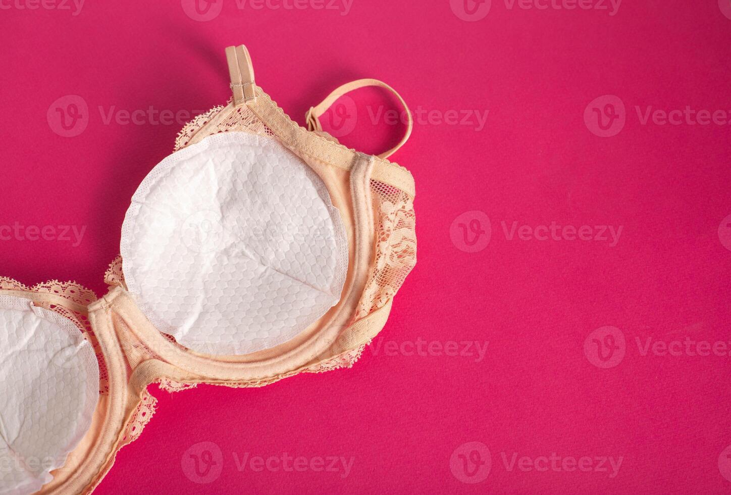 Women's bra with liners against the flow of milk from the breast of a nursing woman on a pink background. Copy space for text photo