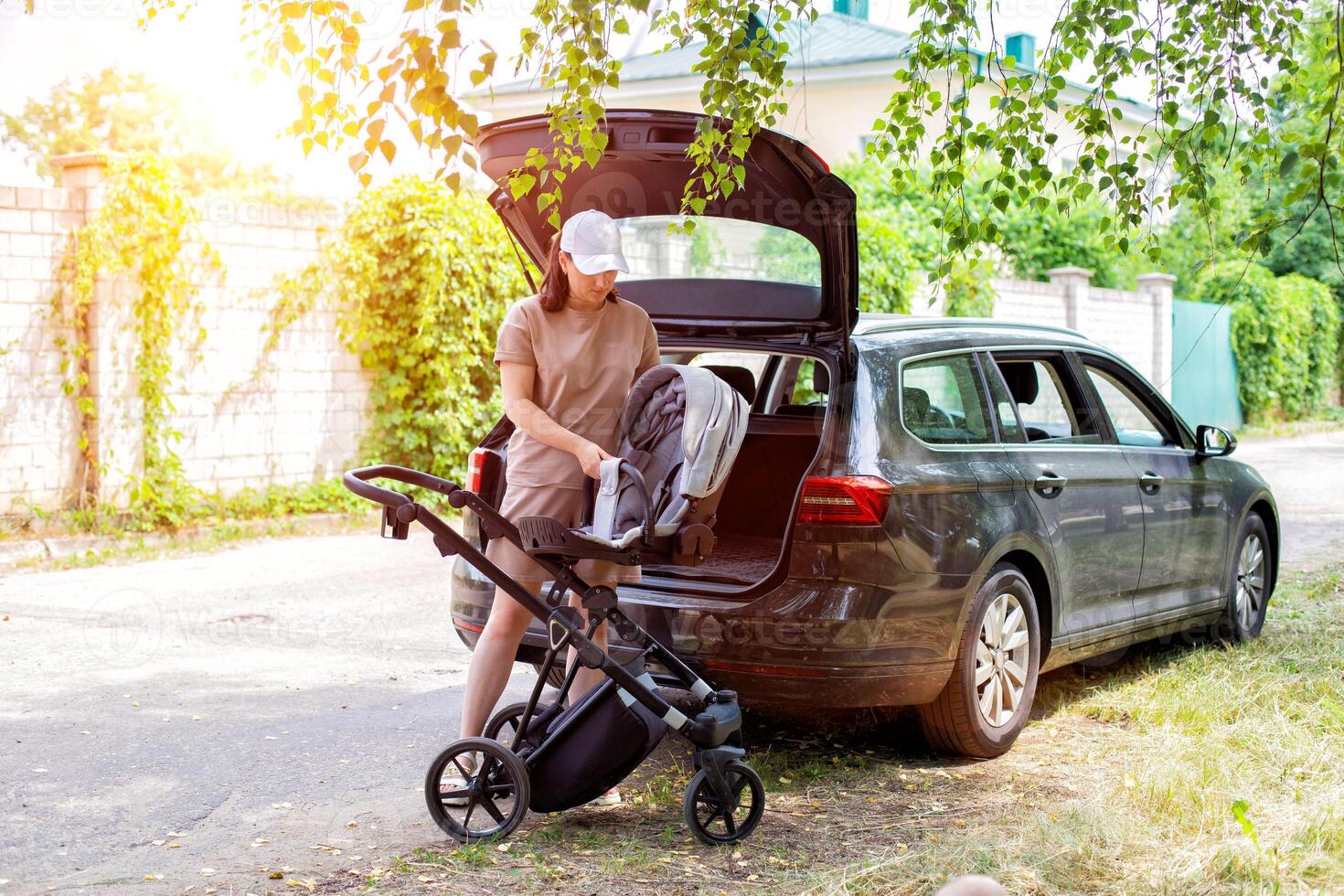 A beautiful girl puts a baby stroller into the open trunk of a car. Traveling in a family car. Copy space for text photo