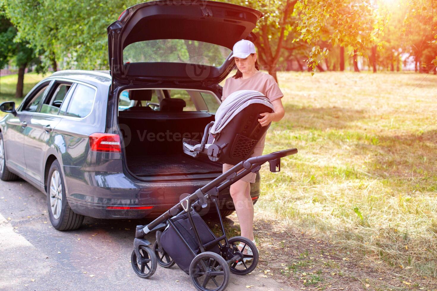 A beautiful girl puts a baby stroller into the open trunk of a car. Traveling in a family car. Copy space for text photo