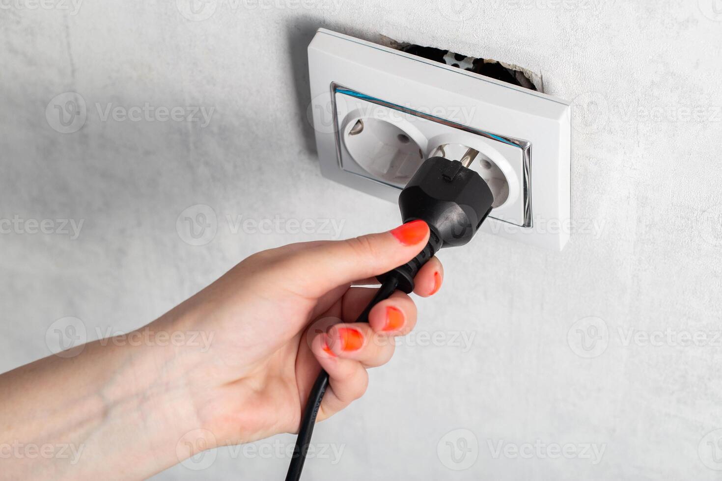 The girl puts the electric plug into a broken socket. Risk of electric shock, close-up photo