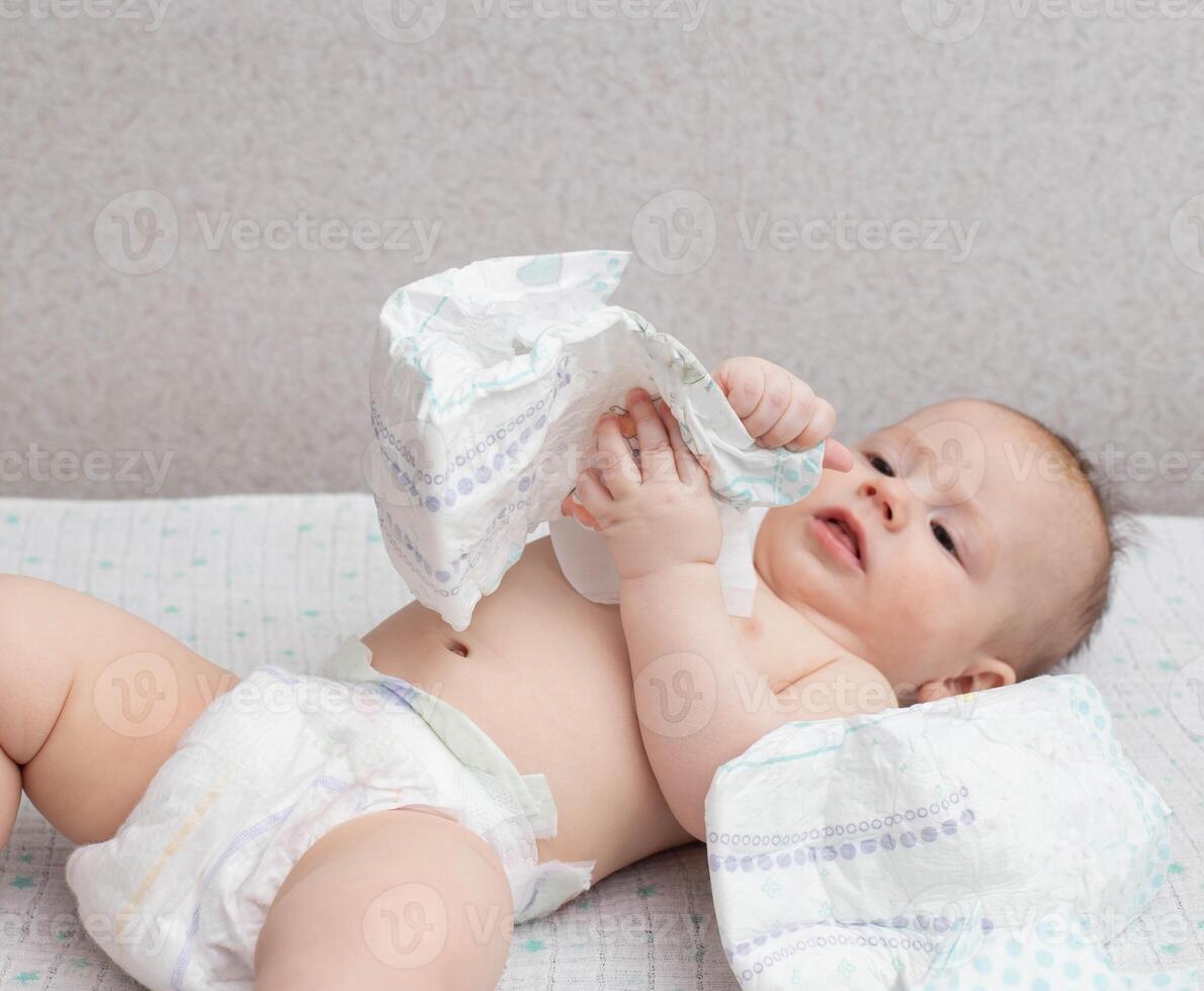 A baby in a diaper lies on a white background plays with a stack of diapers. Copy space for text photo