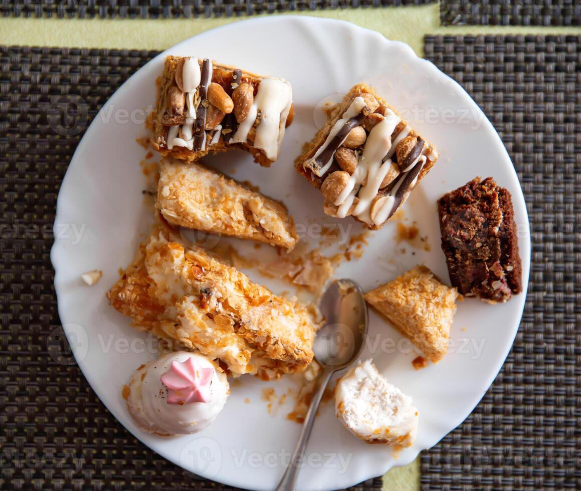 Leftovers in a plate on the table with sweets cakes, close-up photo