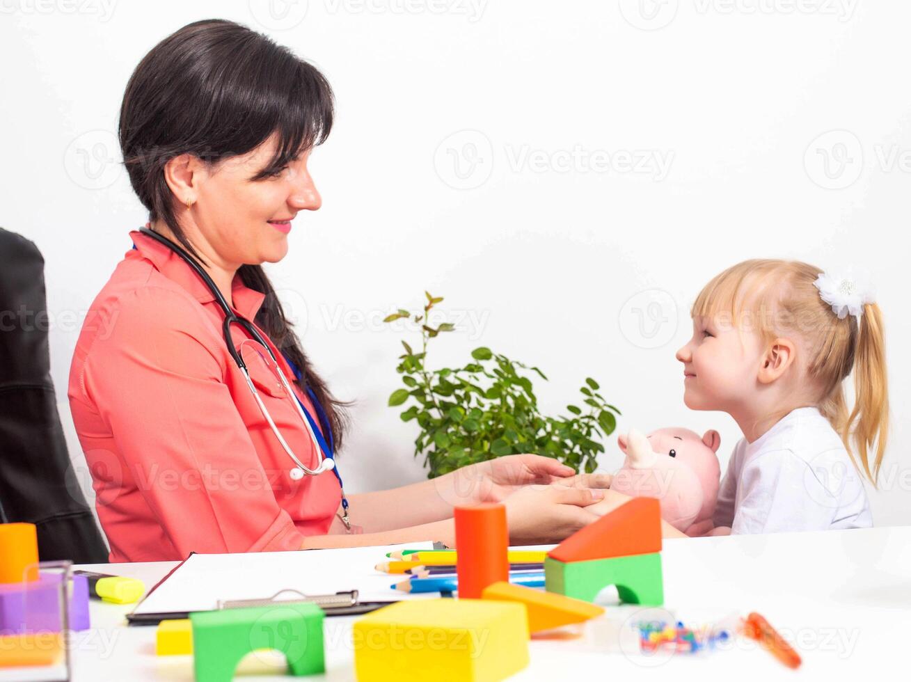 A caucasian woman, a pediatrician, a psychotherapist, is making contact with a girl patient, a child of 3-4 years old. Copy space for text photo