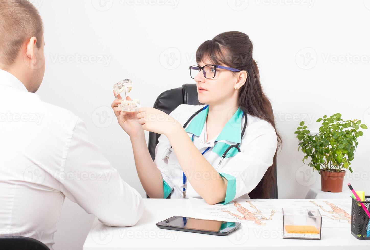 A dentist doctor tells a patient a man on the example of a model of a dental jaw and his disease. The concept of treatment of caries and pulpitis in dentistry using modern methods, copy space photo